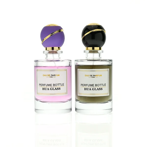 HUA0419 perfume bottle, luxury heavy-base cylindrical glass bottle with high-transparency finish showing colored liquid, featuring a gold-bordered square paper label and a unique round ball plastic cap with a diagonal gold-colored accent stripe, modern elegant fragrance packaging design available in 30ml, 50ml, and 100ml