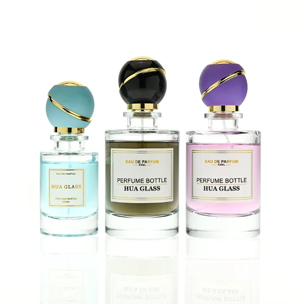 HUA0419 perfume bottle, luxury heavy-base cylindrical glass bottle with high-transparency finish showing colored liquid, featuring a gold-bordered square paper label and a unique round ball plastic cap with a diagonal gold-colored accent stripe, modern elegant fragrance packaging design available in 30ml, 50ml, and 100ml