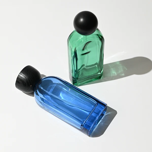 HUA0423 perfume bottle, luxury arch-shaped flat oval glass bottle with translucent finish in green or blue, featuring a dark-colored neck collar and a unique flat-topped glossy black wooden cap, modern elegant fragrance packaging design available in 30ml, 50ml, and 100ml