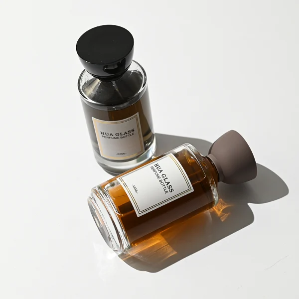 HUA0424 perfume bottle, luxury heavy-base cylindrical glass bottle with translucent deep multi-color finish, featuring a gold-bordered square paper label, a black neck ring, and a unique glossy black tapered cup-shaped plastic cap, modern elegant fragrance packaging design available in 30ml, 50ml, and 100ml