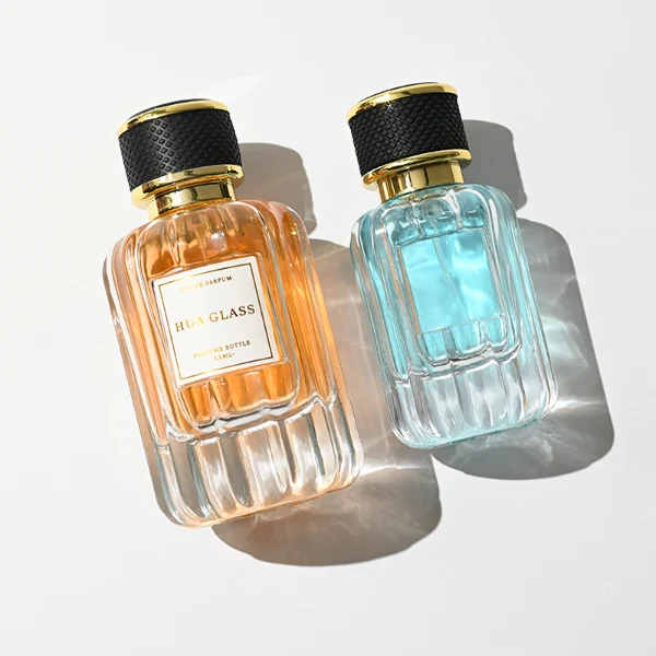 HUA0425 perfume bottle, luxury heavy-base vertical ribbed cylindrical glass bottle with high-transparency finish showing colored liquid, featuring a gold-bordered square paper label and a black textured leather-wrapped plastic cap with gold-colored trim, modern elegant fragrance packaging design available in 30ml, 50ml, and 100ml