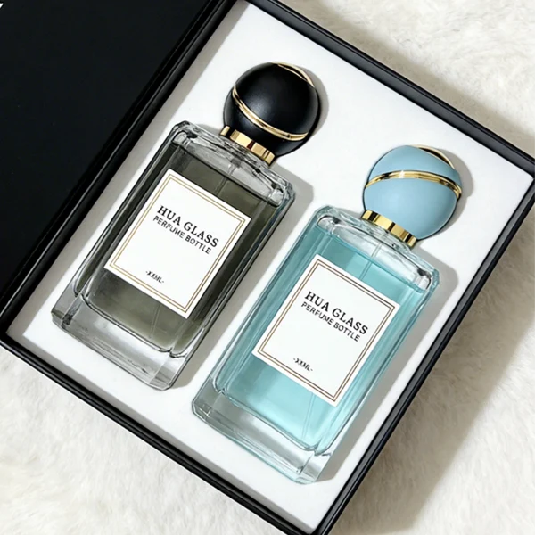 HUA0426 perfume bottle, luxury heavy-base rectangular square glass bottle with high-transparency finish showing colored liquid, featuring a gold-bordered square paper label and a unique round ball plastic cap with a diagonal gold-colored accent stripe, modern elegant fragrance packaging design available in 30ml, 50ml, and 100ml
