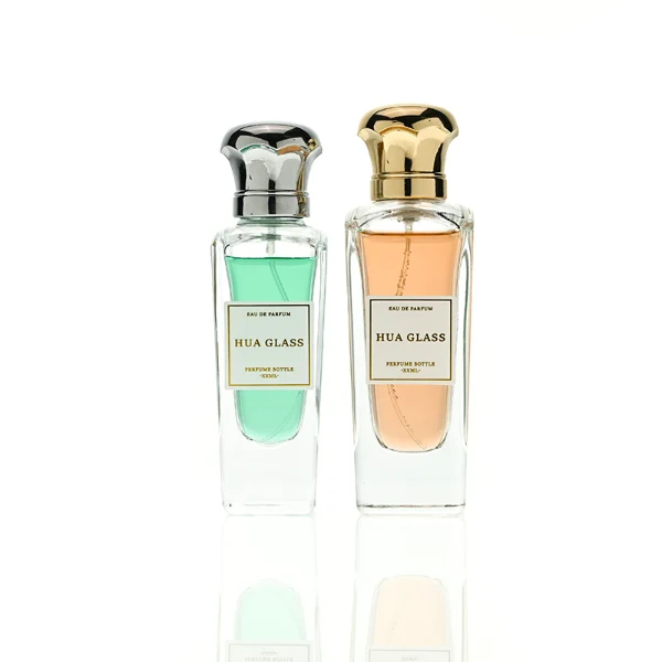 HUA0427 perfume bottle, luxury heavy-base tapered faceted glass bottle with high-transparency finish showing colored liquid, featuring a gold-bordered square paper label and a unique wavy crown-shaped zamak cap with a high-shine gold or silver finish, modern elegant fragrance packaging design available in 50ml and 75ml