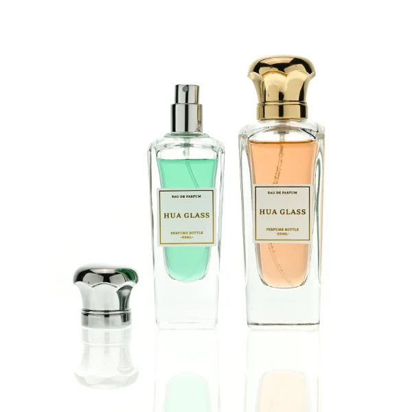 HUA0427 perfume bottle, luxury heavy-base tapered faceted glass bottle with high-transparency finish showing colored liquid, featuring a gold-bordered square paper label and a unique wavy crown-shaped zamak cap with a high-shine gold or silver finish, modern elegant fragrance packaging design available in 50ml and 75ml