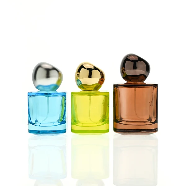HUA0429 perfume bottle, luxury heavy-base round cylindrical glass bottle with high-transparency colorful finish showing blue, green, or brown liquid, featuring a unique irregular pebble-shaped plastic cap with a mirror-shine metallic chrome finish, modern artistic fragrance packaging design available in 30ml, 50ml, and 100ml