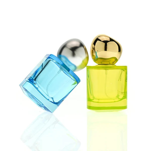 HUA0429 perfume bottle, luxury heavy-base round cylindrical glass bottle with high-transparency colorful finish showing blue, green, or brown liquid, featuring a unique irregular pebble-shaped plastic cap with a mirror-shine metallic chrome finish, modern artistic fragrance packaging design available in 30ml, 50ml, and 100ml