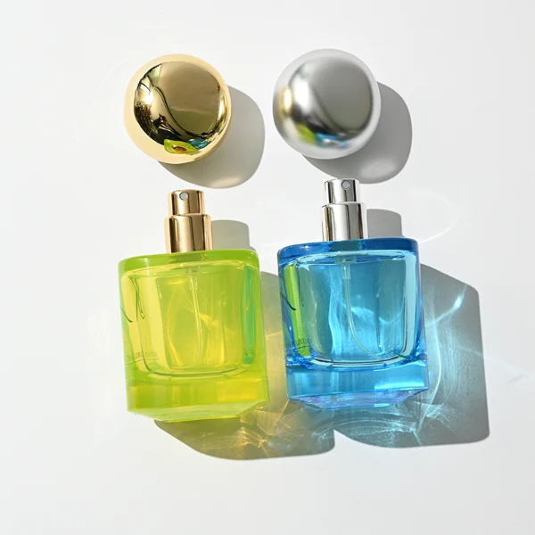 HUA0429 perfume bottle, luxury heavy-base round cylindrical glass bottle with high-transparency colorful finish showing blue, green, or brown liquid, featuring a unique irregular pebble-shaped plastic cap with a mirror-shine metallic chrome finish, modern artistic fragrance packaging design available in 30ml, 50ml, and 100ml