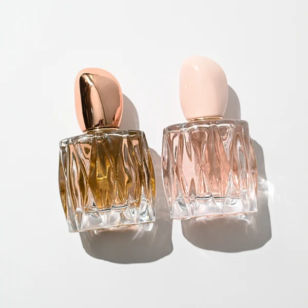 HUA0432 perfume bottle, luxury heavy-base rounded square glass bottle with wavy sculpted embossed patterns and high-transparency clear finish, featuring a unique irregular pebble-shaped plastic cap with a mirror-shine glossy rose gold finish, modern elegant fragrance packaging design