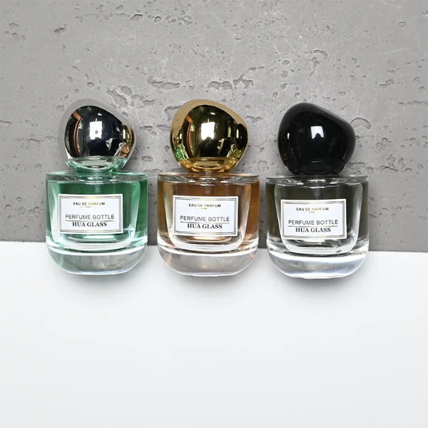 HUA0433 perfume bottle, luxury heavy-base round cylindrical glass bottle with translucent deep multi-color finish, featuring a bordered square paper label and a unique irregular pebble-shaped plastic cap in a glossy black finish, modern artistic fragrance packaging design available in 50ml and 100ml
