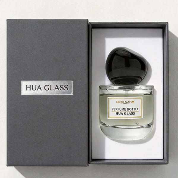 HUA0433 perfume bottle, luxury heavy-base round cylindrical glass bottle with translucent deep multi-color finish, featuring a bordered square paper label and a unique irregular pebble-shaped plastic cap in a glossy black finish, modern artistic fragrance packaging design available in 50ml and 100ml