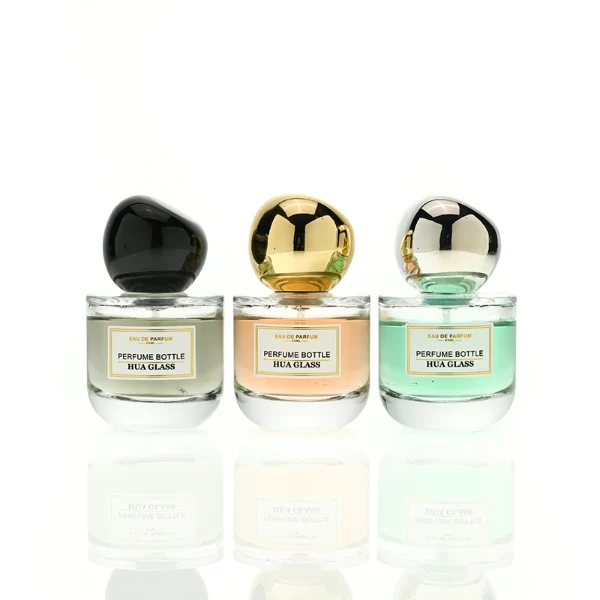 HUA0433 perfume bottle, luxury heavy-base round cylindrical glass bottle with translucent deep multi-color finish, featuring a bordered square paper label and a unique irregular pebble-shaped plastic cap in a glossy black finish, modern artistic fragrance packaging design available in 50ml and 100ml
