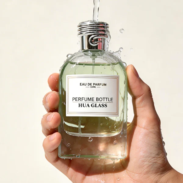 HUA0434 perfume bottle, luxury 100ml heavy-base round cylindrical glass bottle with high-transparency clear finish, featuring a bordered square paper label and a unique horizontal threaded cylindrical plastic cap with a mirror-shine metallic chrome finish, modern elegant fragrance packaging design
