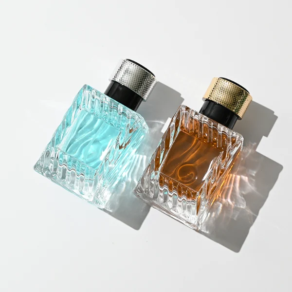 HUA0435 perfume bottle, luxury 50ml angular square glass bottle with wavy sculpted embossed patterns and translucent deep multi-color finish, featuring a metallic gold aluminum label and a glossy black cylindrical plastic cap encased with a textured silver-colored knurled band, modern elegant fragrance packaging design