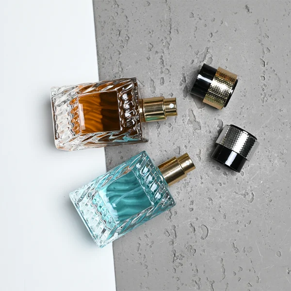 HUA0435 perfume bottle, luxury 50ml angular square glass bottle with wavy sculpted embossed patterns and translucent deep multi-color finish, featuring a metallic gold aluminum label and a glossy black cylindrical plastic cap encased with a textured silver-colored knurled band, modern elegant fragrance packaging design