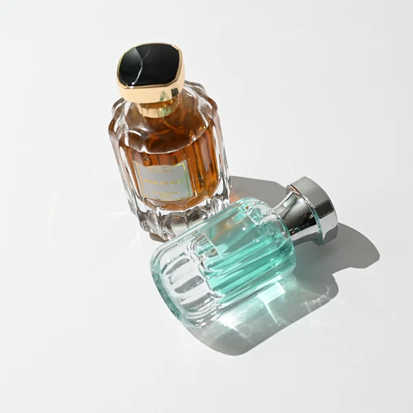 HUA0436 perfume bottle, luxury heavy-base round cylindrical glass bottle with vertical fluted sculpted patterns and high-transparency clear finish, featuring a bordered square paper label and a flared hourglass solid Zamak cap with a mirror-shine glossy finish, modern elegant fragrance packaging design available in 30ml, 50ml, and 100ml