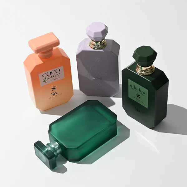 HUA0443 perfume bottle showcases a square angular glass body in vibrant frosted, solid, and gradient color options. It is crowned with artistic plastic caps featuring crown, cube, and diamond-cut shapes. Designed for wholesalers, it provides 30ml, 50ml, and 100ml choices, combining aesthetic variety with durable design for diverse fragrance lines.
