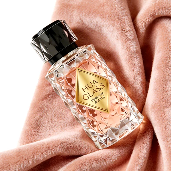 HUA0448 perfume bottle features a textured, diamond-patterned clear glass body paired with a matching cylindrical faceted plastic cap in black, silver, or gold. Designed for wholesalers, it offers 50ml and 100ml options, combining an elegant geometric design with practical durability for premium fragrance lines.