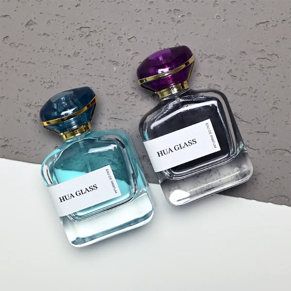HUA0449 perfume bottle features a rounded short, thick-bottom square clear glass body paired with a unique organic, abstract-shaped translucent cap with a gold collar. Designed for wholesalers, it offers a 100ml capacity option, blending a modern minimalist profile with structural durability for distinct fragrance collections.