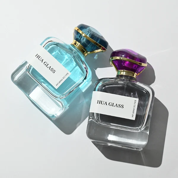HUA0449 perfume bottle features a rounded short, thick-bottom square clear glass body paired with a unique organic, abstract-shaped translucent cap with a gold collar. Designed for wholesalers, it offers a 100ml capacity option, blending a modern minimalist profile with structural durability for distinct fragrance collections.