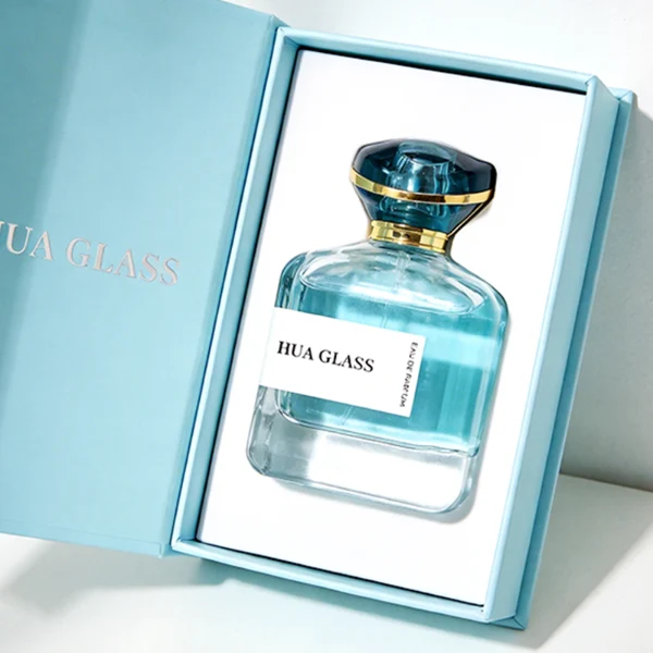 HUA0449 perfume bottle features a rounded short, thick-bottom square clear glass body paired with a unique organic, abstract-shaped translucent cap with a gold collar. Designed for wholesalers, it offers a 100ml capacity option, blending a modern minimalist profile with structural durability for distinct fragrance collections.