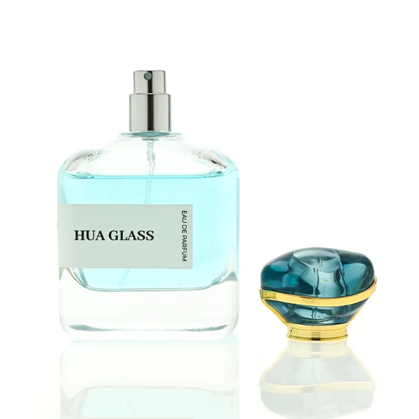 HUA0449 perfume bottle features a rounded short, thick-bottom square clear glass body paired with a unique organic, abstract-shaped translucent cap with a gold collar. Designed for wholesalers, it offers a 100ml capacity option, blending a modern minimalist profile with structural durability for distinct fragrance collections.