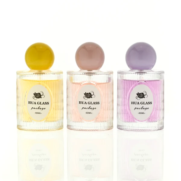 HUA0450 perfume bottle features a clear cylindrical glass body with vertical ribbed grooves, paired with a smooth spherical ball-shaped plastic cap in purple, pink, or yellow. Designed for wholesalers, it offers a 50ml capacity option, combining an elegant textured profile with structural durability for distinct fragrance lines.