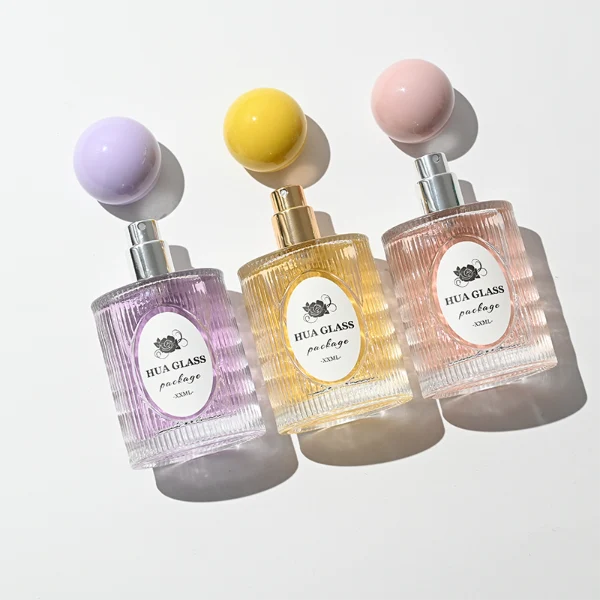 HUA0450 perfume bottle features a clear cylindrical glass body with vertical ribbed grooves, paired with a smooth spherical ball-shaped plastic cap in purple, pink, or yellow. Designed for wholesalers, it offers a 50ml capacity option, combining an elegant textured profile with structural durability for distinct fragrance lines.