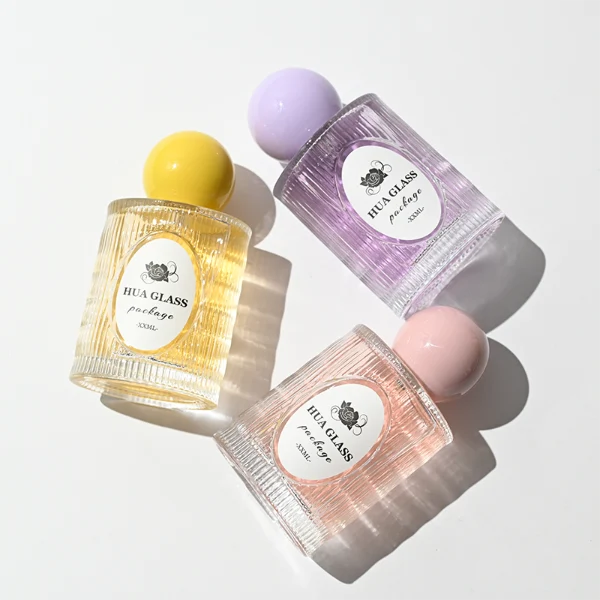 HUA0450 perfume bottle features a clear cylindrical glass body with vertical ribbed grooves, paired with a smooth spherical ball-shaped plastic cap in purple, pink, or yellow. Designed for wholesalers, it offers a 50ml capacity option, combining an elegant textured profile with structural durability for distinct fragrance lines.