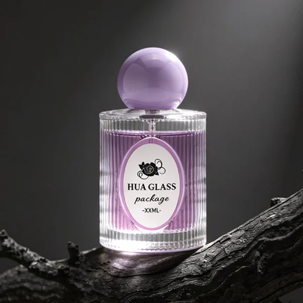 HUA0450 perfume bottle features a clear cylindrical glass body with vertical ribbed grooves, paired with a smooth spherical ball-shaped plastic cap in purple, pink, or yellow. Designed for wholesalers, it offers a 50ml capacity option, combining an elegant textured profile with structural durability for distinct fragrance lines.