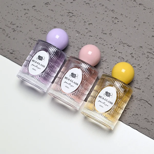HUA0450 perfume bottle features a clear cylindrical glass body with vertical ribbed grooves, paired with a smooth spherical ball-shaped plastic cap in purple, pink, or yellow. Designed for wholesalers, it offers a 50ml capacity option, combining an elegant textured profile with structural durability for distinct fragrance lines.