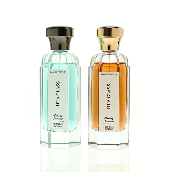 two tall clear hexagonal glass perfume bottles hold teal and amber liquids. The left bottle has a glossy silver cap, while the right bottle is topped with a polished gold cap.
