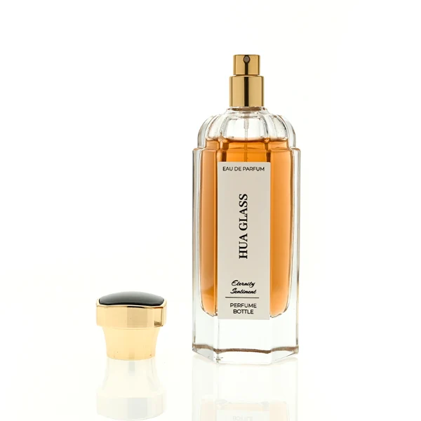 two tall clear hexagonal glass perfume bottles hold teal and amber liquids. The left bottle has a glossy silver cap, while the right bottle is topped with a polished gold cap.