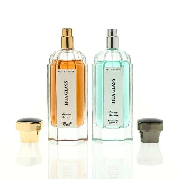 two tall clear hexagonal glass perfume bottles hold teal and amber liquids. The left bottle has a glossy silver cap, while the right bottle is topped with a polished gold cap.