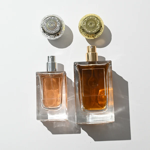 HUA0454 perfume bottle showcases a clear, thick-walled rectangular glass body with an ornate, textured round plastic cap in gold or silver. Designed for wholesalers, it offers 50ml and 100ml capacities, combining a sleek angular profile with a highly decorative cap style.