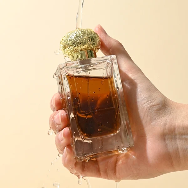HUA0454 perfume bottle showcases a clear, thick-walled rectangular glass body with an ornate, textured round plastic cap in gold or silver. Designed for wholesalers, it offers 50ml and 100ml capacities, combining a sleek angular profile with a highly decorative cap style.