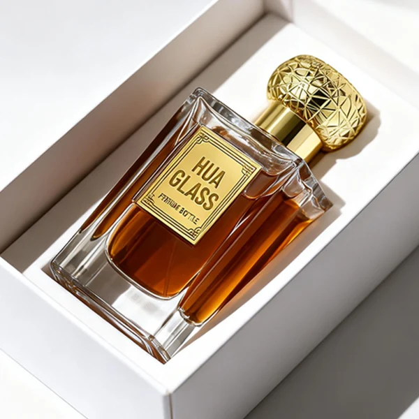 HUA0454 perfume bottle showcases a clear, thick-walled rectangular glass body with an ornate, textured round plastic cap in gold or silver. Designed for wholesalers, it offers 50ml and 100ml capacities, combining a sleek angular profile with a highly decorative cap style.