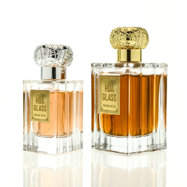 HUA0454 perfume bottle showcases a clear, thick-walled rectangular glass body with an ornate, textured round plastic cap in gold or silver. Designed for wholesalers, it offers 50ml and 100ml capacities, combining a sleek angular profile with a highly decorative cap style.
