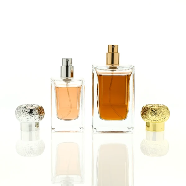 HUA0454 perfume bottle showcases a clear, thick-walled rectangular glass body with an ornate, textured round plastic cap in gold or silver. Designed for wholesalers, it offers 50ml and 100ml capacities, combining a sleek angular profile with a highly decorative cap style.