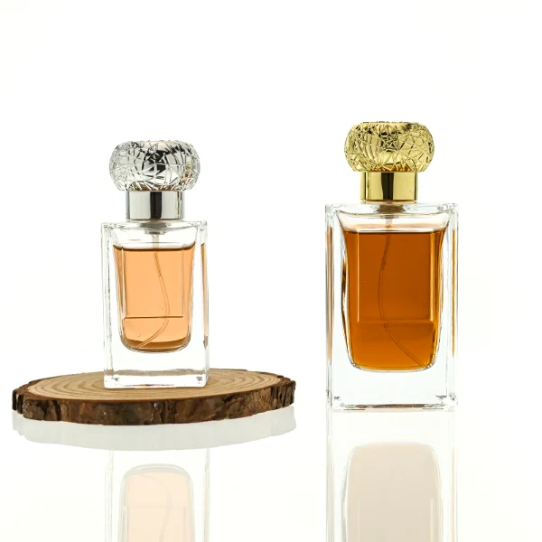 HUA0454 perfume bottle showcases a clear, thick-walled rectangular glass body with an ornate, textured round plastic cap in gold or silver. Designed for wholesalers, it offers 50ml and 100ml capacities, combining a sleek angular profile with a highly decorative cap style.