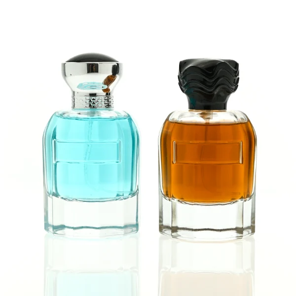 In the provided image, two clear Cylindrical  glass perfume bottles with thick bases stand side by side, containing light blue and amber liquids. The left bottle is topped with a smooth, flared silver cap with a textured collar, while the right bottle is topped with a unique, textured wavy black cap.