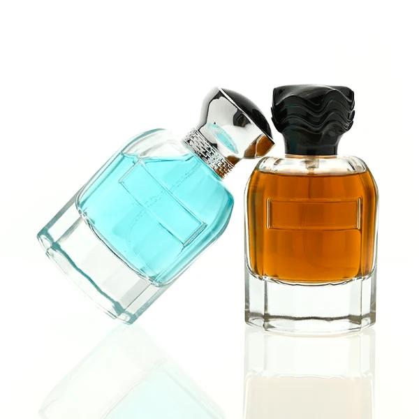 In the provided image, two clear Cylindrical glass perfume bottles with thick bases stand side by side, containing light blue and amber liquids. The left bottle is topped with a smooth, flared silver cap with a textured collar, while the right bottle is topped with a unique, textured wavy black cap.