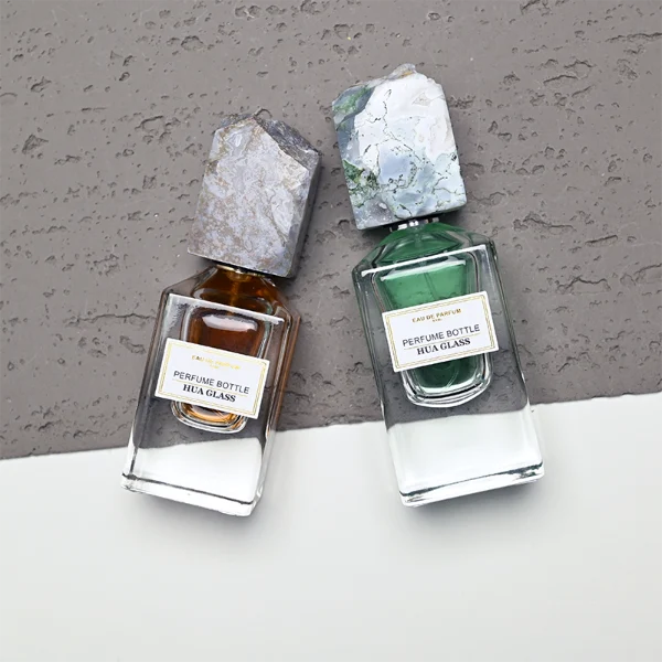HUA0457 perfume bottle showcases a clear, thick-bottomed rectangular glass frame paired with a striking, unique block cap made of raw natural stone. Designed for premium wholesale markets, it offers 30ml and 50ml options, combining an organic elemental style with architectural structural durability.