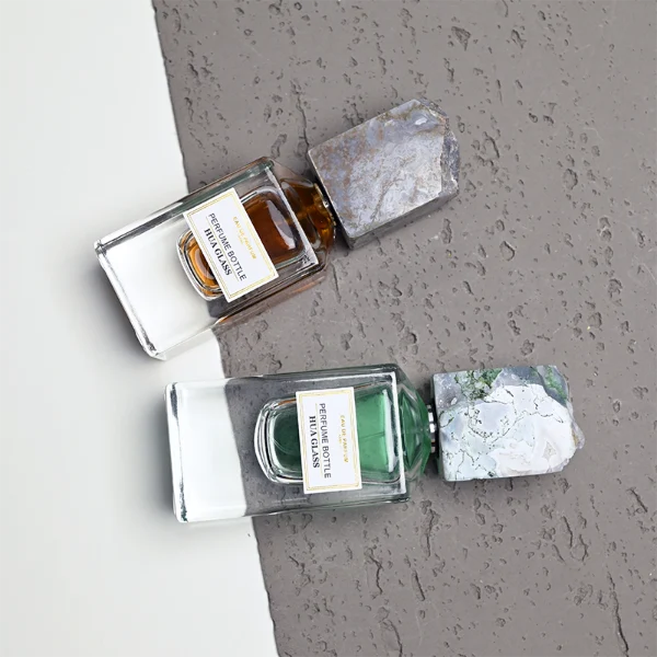 HUA0457 perfume bottle showcases a clear, thick-bottomed rectangular glass frame paired with a striking, unique block cap made of raw natural stone. Designed for premium wholesale markets, it offers 30ml and 50ml options, combining an organic elemental style with architectural structural durability.