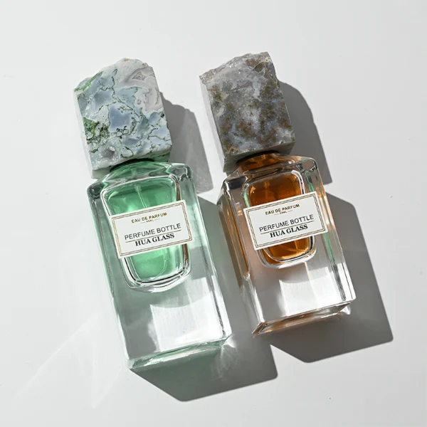 HUA0457 perfume bottle showcases a clear, thick-bottomed rectangular glass frame paired with a striking, unique block cap made of raw natural stone. Designed for premium wholesale markets, it offers 30ml and 50ml options, combining an organic elemental style with architectural structural durability.