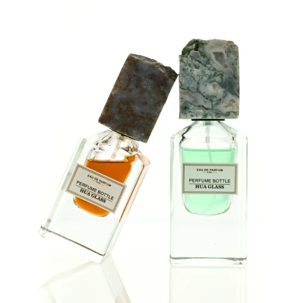 HUA0457 perfume bottle showcases a clear, thick-bottomed rectangular glass frame paired with a striking, unique block cap made of raw natural stone. Designed for premium wholesale markets, it offers 30ml and 50ml options, combining an organic elemental style with architectural structural durability.