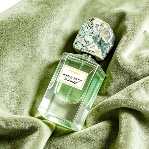 HUA0457 perfume bottle showcases a clear, thick-bottomed rectangular glass frame paired with a striking, unique block cap made of raw natural stone. Designed for premium wholesale markets, it offers 30ml and 50ml options, combining an organic elemental style with architectural structural durability.