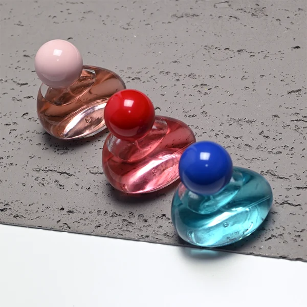 HUA0460 perfume bottle features an asymmetrical, organic pebble-shaped clear glass body paired with a glossy spherical ball cap in blue, red, or pink, it offers a 50ml capacity option, blending a playful geometric profile with high wholesale utility.