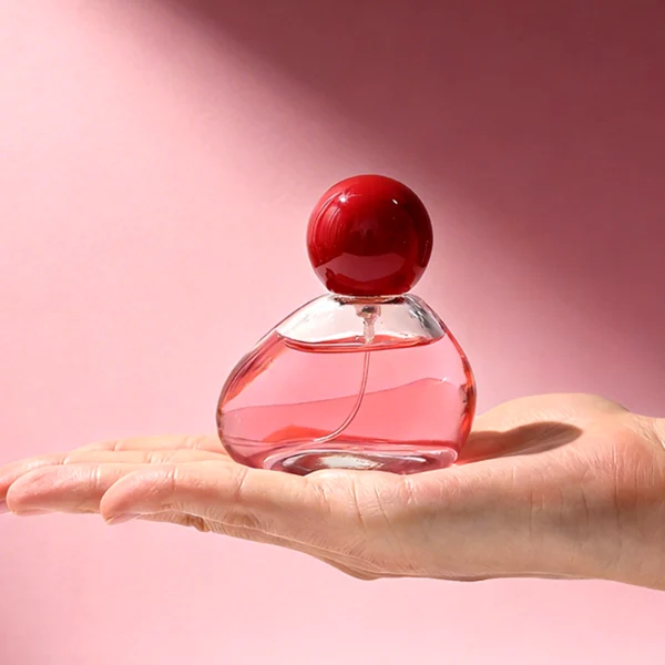 HUA0460 perfume bottle features an asymmetrical, organic pebble-shaped clear glass body paired with a glossy spherical ball cap in blue, red, or pink, it offers a 50ml capacity option, blending a playful geometric profile with high wholesale utility.