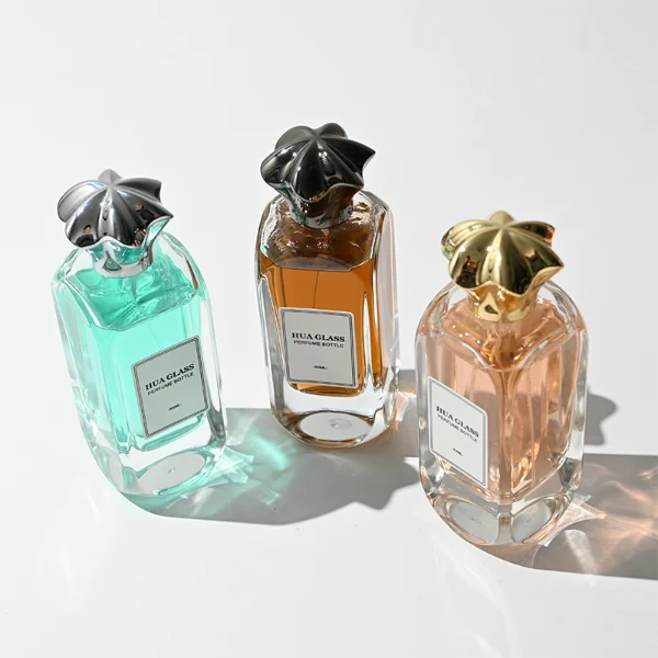 A luxury rectangular perfume bottle featuring a thick, rounded clear glass base and a heavy metallic crown-shaped Zamac cap in gold, silver, or black.