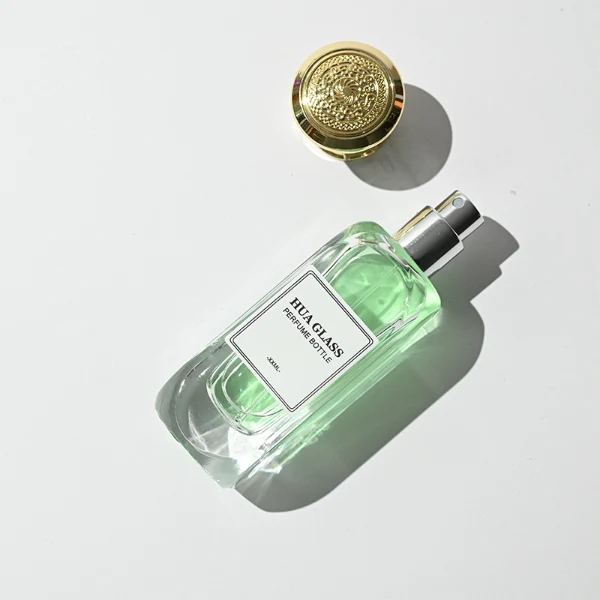 A luxury rectangular perfume bottle featuring a thick, rounded clear glass base and a heavy metallic crown-shaped Zamac cap in gold, silver, or black.